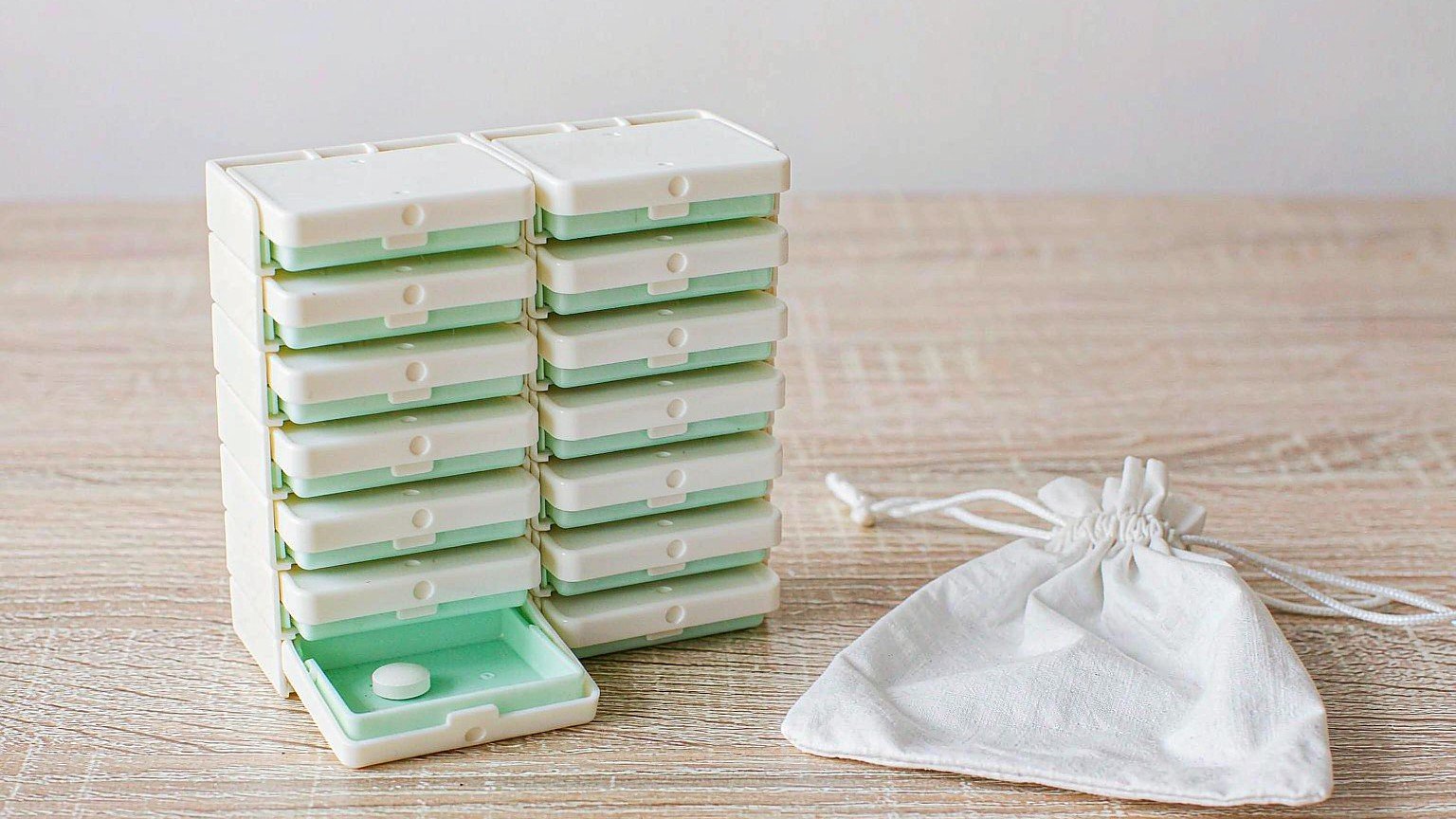 White weekly pill organizer with individual flip-lid compartments and a plain white storage pouch, a moisture-proof design