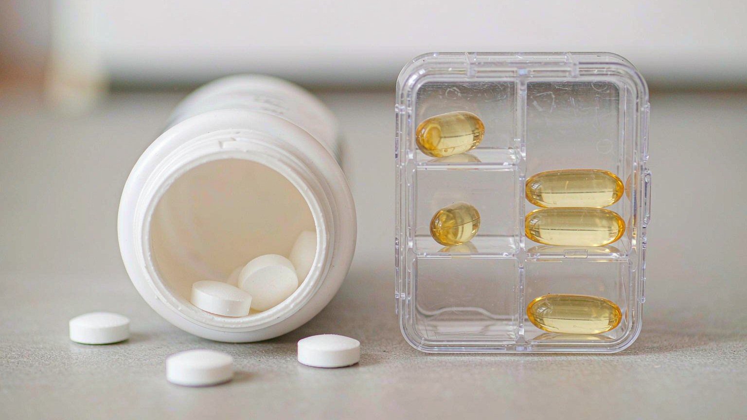 Effervescent tablets in a sealed tube and a softgel capsule beside a clear pill organizer compartment