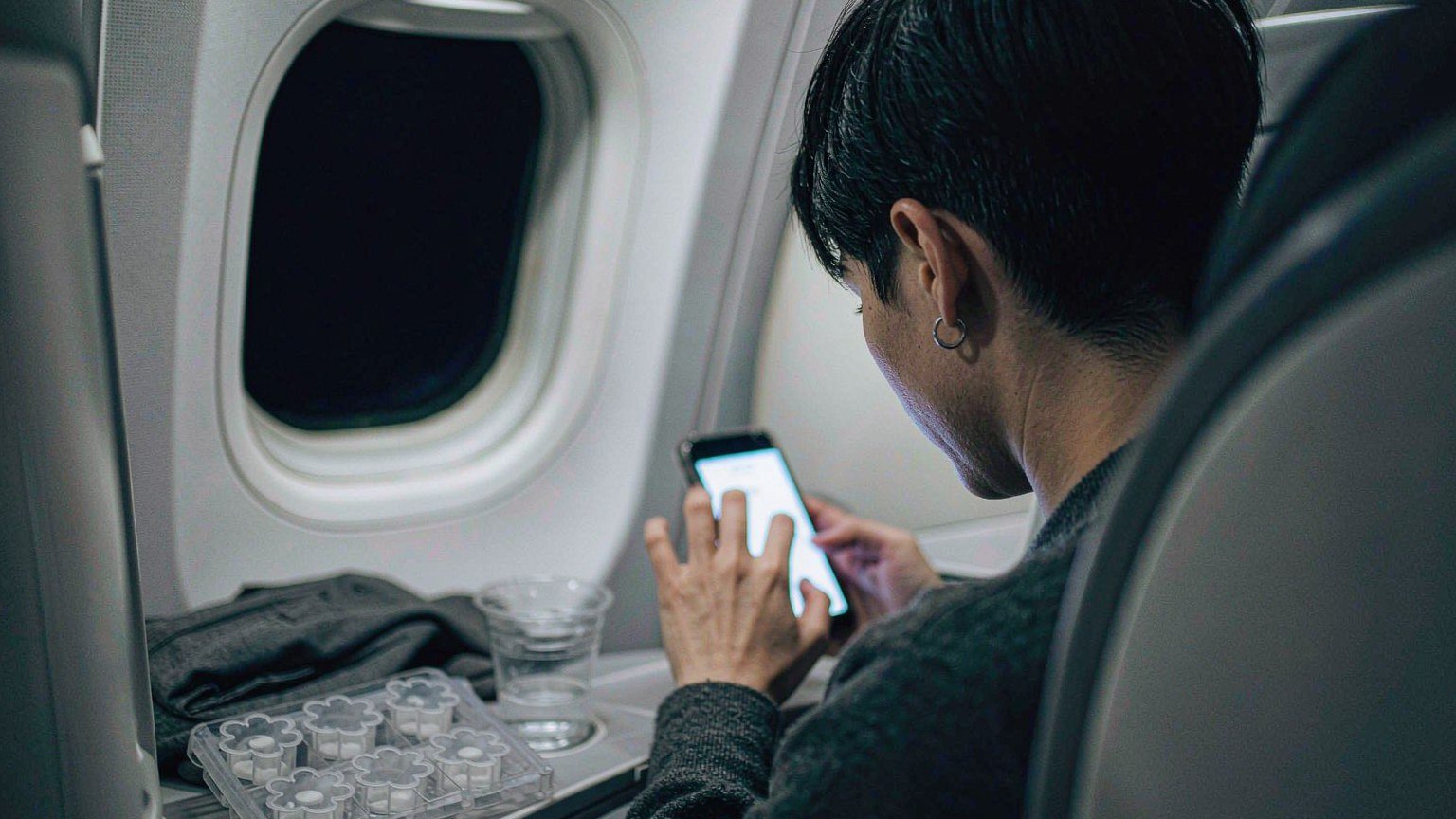 A traveler by an airplane window at night with a small pill organizer on the tray table, keeping medication on schedule across cities